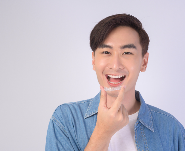 Smiling man holding a clear Invisalign aligner